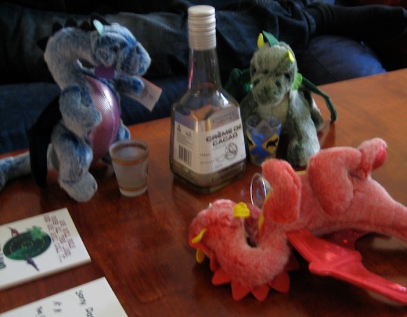Three plush dragons grouped around a mostly empty bottle of Advocat and several shot glasses
