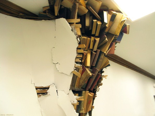 Photograph of a wall that has broken open ostensibly under the weight of a pile of books