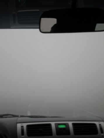 view from interior of car of a street disappearing into fog a couple of metres from the bumper