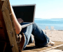 girl sitting on a reclining hair, laptop in lap, beach and sea in the background