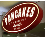 Picture of restaurant sign. Maroon oval shape with white text: PANCAKES at Carillon. Est. 1983.