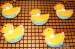 Cookies in the shape of ducklings with a line of blue at the bottom as though they are swimming.