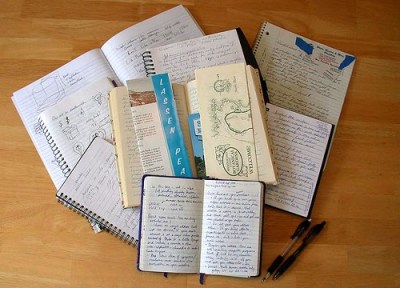 Pile of open hand written and hand drawn notebooks.