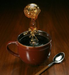 Cup of black coffee on a wooden table with a dramatic splash of coffee above it.