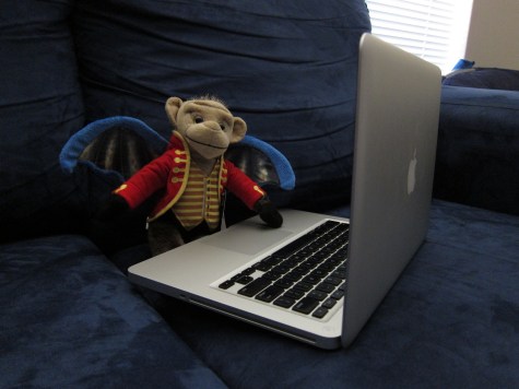 Foot-high Chistery (flying monkey from Wizard of Oz) sitting on a blue couch with a laptop on his lap.