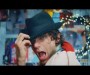 Screencap from Mika's music video of "We Are Golden". Mika is wrapped in a flag, posing with a black hat and singing.