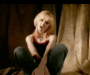 Screenshot from the music video. Merril Bainbridge sitting cross-legged in jeans and a black and red singlet.