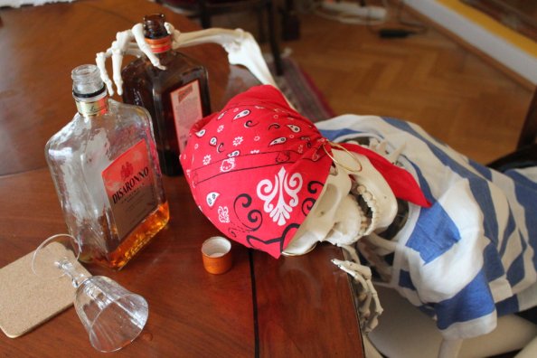 Skeleton dressed as a pirate, slumped over a table, one hand still wrapped around one of the mostly empty bottles of alcohol arrayed in front of him. Or her. But probably him.