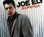 Record cover of Joe Ely's 'Musta Notta Gotta Lotta". Features the singer himself in a grey coat standing in front of a corrugated iron wall.
