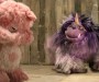 Pink teddy cowers from purple fanged and horned muppet as they face off in cock-fighting ring.
